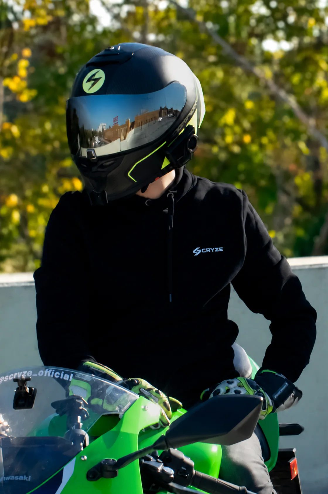 SCRYZE mit Helm auf einem grünen Motorrad sitzend