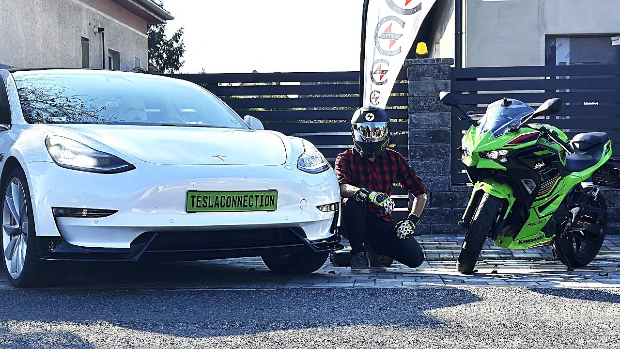 SCRYZE mit Helm, hockend zwischen einem weißen Tesla und einem grünen Kawasaki-Motorrad